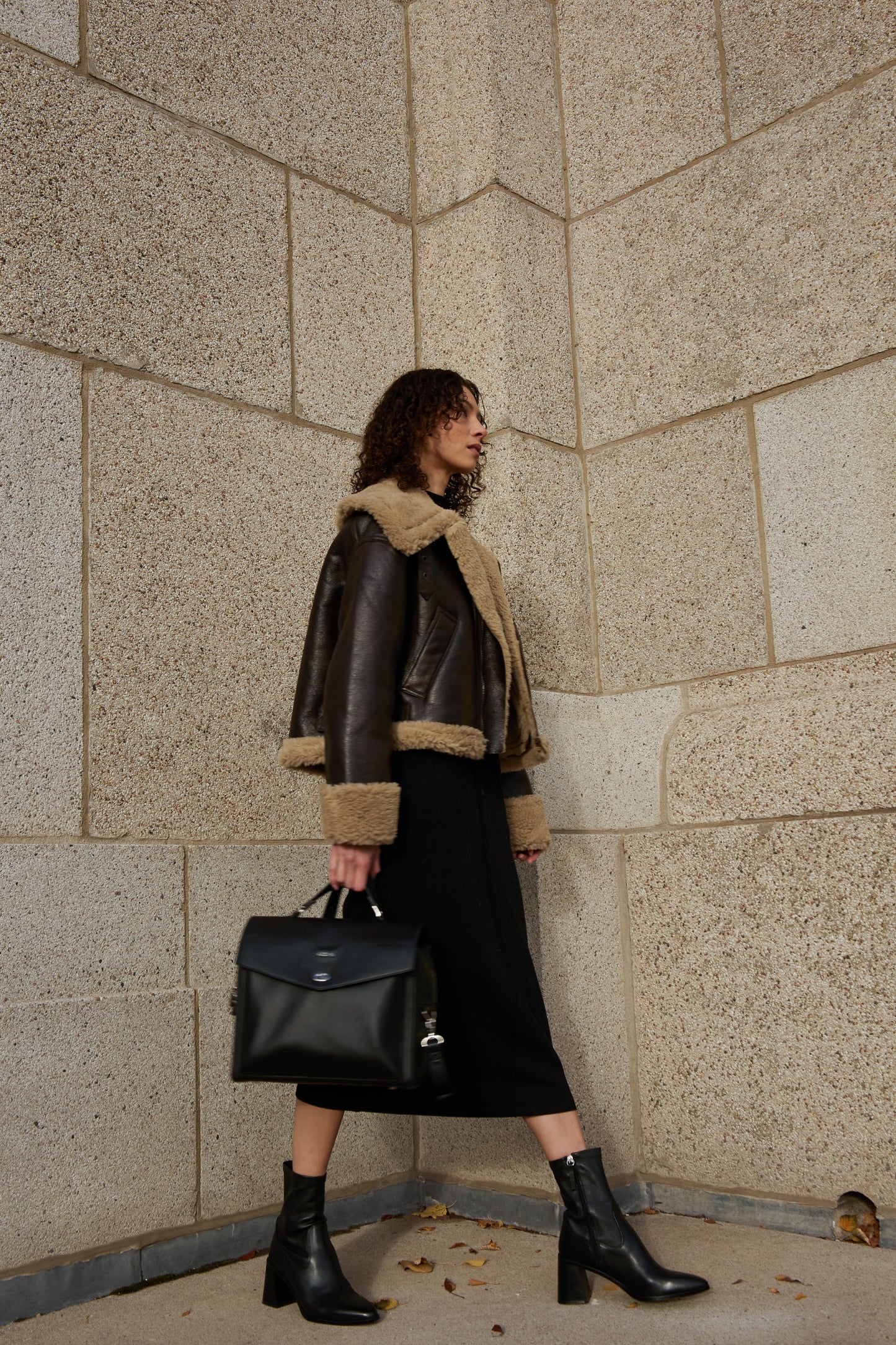 black vegan leather lunch bag with silver hardware being held by model in chic dark toned outfit outside by heritage stone building walking to work